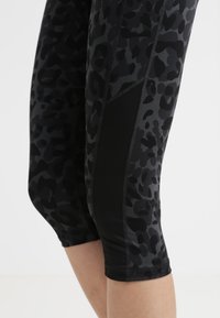 Ingrandimento di gambe che indossano leggings leopardati neri e grigi scuri con pannelli neri solidi sui lati, accorciati sotto le ginocchia.