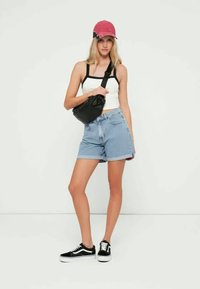 Svart midjevektpose, hvit singlet, denimshorts og svarte joggesko med hvite såler. Rosa caps med taggete kantdetalj. Enkelt, avslappet antrekk.