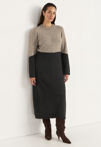 Lång, långärmad klänning i en beige och svart färgblockdesign. Tillverkad av mjukt tyg med rund halsringning och strukturella ytdetaljer.