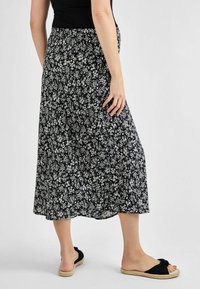 Jupe midi noire à fleurs avec une taille smockée, ornée de motifs de fleurs blanches. Associée à des sandales à glisser noires, offrant un look décontracté.