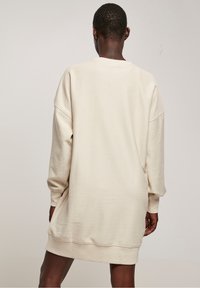 Robe-pull côtelée crème avec manches longues, coupe ample et encolure ronde, présentant une couleur unie et une texture douce.