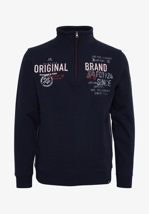 Tumed sinine fliiste sviiter pooltõmblukuga kraes. Omab valget ja punast teksti, tekstuuriga mustri aktsente ning soonikkoes varrukaid.