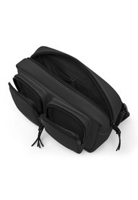 Svart väska med slät, matt yta, med en huvudfack med dragkedja och två framfickor. Accentuerad med kontrasterande vit sömnad.