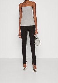 Srebrny top bez ramiączek z peplum, połączony z czarnymi spodniami slim fit z bocznymi rozcięciami. Modelka trzyma metaliczną torebkę i nosi szpilki.