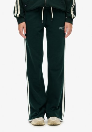 Pantalons de survêtement verts en tissu doux, dotés de rayures latérales blanches et d'une taille élastique avec un cordon de serrage. "ATHLÈTE" imprimé sur le devant.