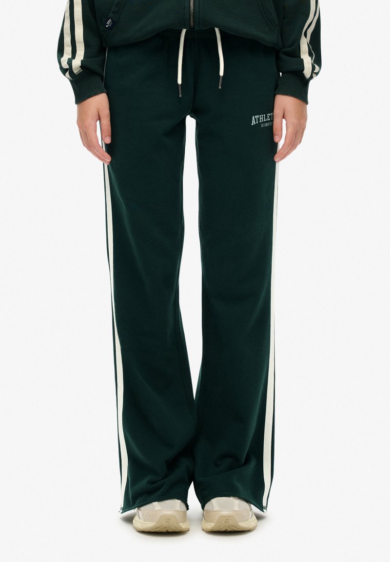 Grüne Sweatpants aus weichem Stoff, mit weißen Seitenstreifen und einem elastischen Bund mit Kordelzug. "ATHLETE" auf der Vorderseite aufgedruckt.