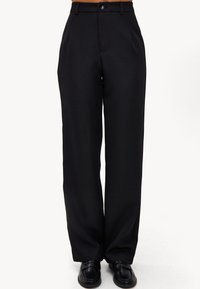 Pantalons larges noirs en tissu lisse, dot�és d'une fermeture à un bouton, de poches avant et d'une coupe ajustée.