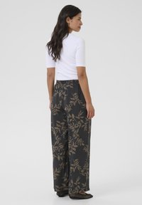 Wide-leg trousers in dark fabric featuring a gold leaf pattern. Elastic waistband and side pockets, paired with a fitted white shirt.