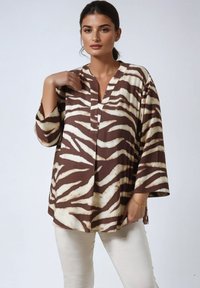 Brown and beige patterned tunic with a V-neck and wide sleeves, made of soft fabric, featuring a bold zebra-stripe design.