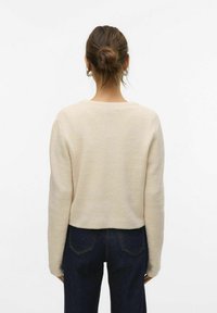 Lichtbeige cropped sweater met lange mouwen en een brede halslijn, gecombineerd met donkere denim. Zachte textuur zichtbaar.