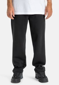 Czarne dresy o luźnym kroju, wykonane z miękkiego materiału, w połączeniu z czarnymi sneakrsami z teksturowanymi sznurowadłami i amortyzowaną podeszwą.