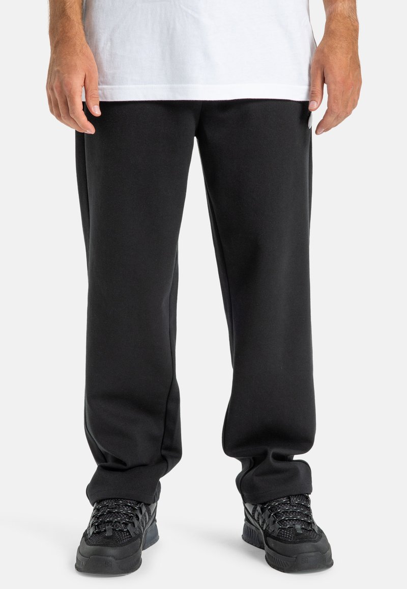 Czarne dresy o luźnym kroju, wykonane z miękkiego materiału, w połączeniu z czarnymi sneakrsami z teksturowanymi sznurowadłami i amortyzowaną podeszwą.