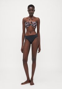 Musta bikinit, joissa on kukkakuosiset bandeau-yksityiskohdat ja pilkkukuosiset alaosat. Silkkinen kangas, istuva malli ja niskalenkit.
