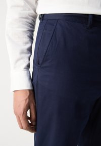 Mørkeblå bukser med strukturert stoff, med sidelommer og slim fit, kombinert med en hvit langermet skjorte.