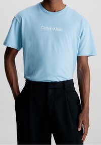 Světle modré bavlněné tričko s krátkým rukávem a kulatým výstřihem, na hrudi s bílým textovým logem "Calvin Klein".