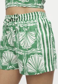 Πράσινες και λευκές σορτς με μοτίβα κοχυλιών και ρίγες, ελαστική μέση και κορδόνι, φορεμένες με ταιριαστό cropped τοπ.