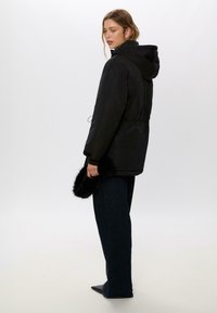 Čierna parka bunda so zateplením z umelého kožušiny a s kapucňou, s nastaviteľným pásom, postrannými vreckami a dlhými rukávmi. Spárovaná s tmavomodrými širokými nohavicami.