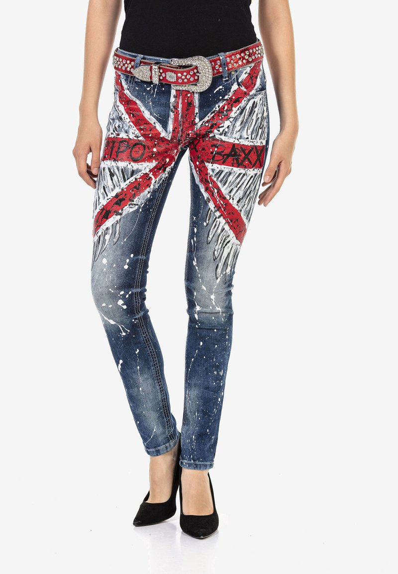 Blaue Jeans aus Denim mit einem Union Jack-Muster in Rot und Weiß. Der Bund ist mit einem genoppten roten Gürtel mit einer metallischen Schnalle versehen.