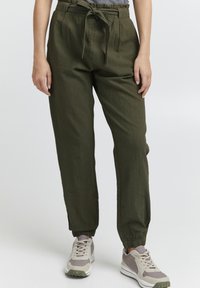 Olive green, lightweight pants with a high waist, pleated front, and drawstring tie. Cuffed ankles provide a tapered fit. Paired with gray and white sneakers.