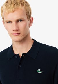 Donkerblauwe polo met een klassieke kraag, gemaakt van gebreide stof, met twee knopen en een klein groen-wit krokodillenlogo op de borst.