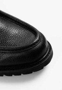 Zapato de cuero negro con un acabado texturizado, puntera redonda y suela resistente contrastante. Presenta costuras visibles y un detalle de borde liso.