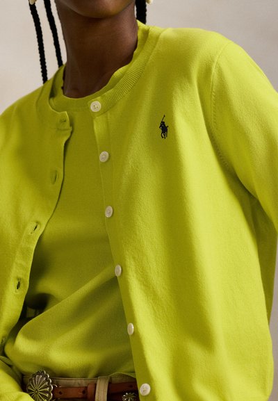 Λαχανί πράσινη ζακέτα από μαλακό πλεκτό ύφασμα, με στρογγυλή λαιμόκοψη, κουμπώματα και μικρή λεπτομέρεια με λογότυπο στο στήθος.