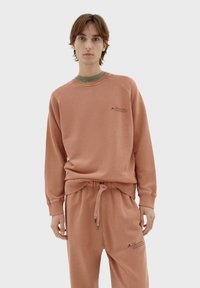Terracotta sweatshirt met geribde ronde hals, lange raglanmouwen en bijpassende jogpants, met een klein bedrukt logo-detail.