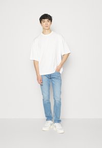 Camiseta blanca de manga corta oversize combinada con vaqueros de mezclilla azul claro y zapatillas blancas. El conjunto presenta un corte relajado y un diseño minimalista.