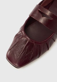 Μαρόν δερμάτινο παπούτσι Mary Jane με στρογγυλεμένη τετράγωνη μύτη, πλισέ σχεδιασμό και λουράκι με διακοσμητικό άνοιγμα στο πέλμα.