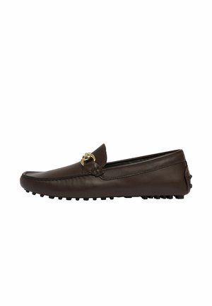 Mocasín de cuero marrón con punta redondeada, adornos de metal dorado y suela texturizada que presenta pequeñas protuberancias para mayor agarre.