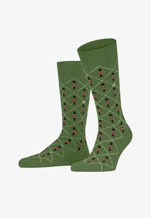 Chaussettes vertes avec des motifs de garde rouges et noirs, présentant un motif en losange souligné de blanc, fabriquées dans un matériau doux et extensible.