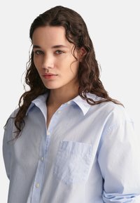 Light blue, long-sleeve button-up shirt with a collar, single chest pocket, and soft texture. Fabric appears slightly wrinkled.