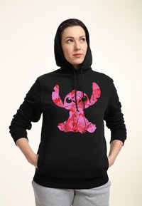Černá mikina s kapucí, která má výraznou růžovou a červenou grafiku stylizované postavy. Měkký materiál s přední kapsou a nastavitelnou kapucí se šňůrkou.