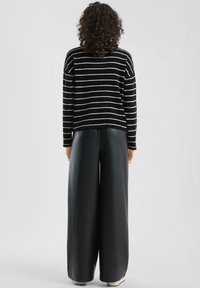 Czarnobiały sweter w paski o luźnym kroju, zestawiony z szerokimi czarnymi skórzanymi spodniami. Miękka faktura, casualowy design i minimalistyczne detale.