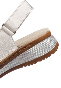 White leather sandal strap with stitched edges attached to a brown and silver textured sole with a ridged bottom.