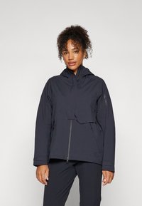 Veste imperméable bleu marine avec fermeture éclair, poignets élastiques et capuche. Dotée d'un design court et de deux poches latérales zippées.
