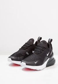 Black athletic shoes with a textured mesh upper, white Nike logo, and Air Max cushioning. Features a synthetic sole and a distinctive design.