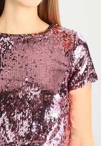 Top a maniche corte ricoperto di paillettes riflettenti rosa e rosa antico, con scollatura tonda e superficie liscia.