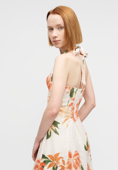 Φλοράλ φόρεμα με μπεζ βάση και πορτοκαλί και πράσινα σχέδια, λαιμός halter με κορδέλα δέσιμο και πλάτη με σούρες για εφαρμοστό σιλουέτα.