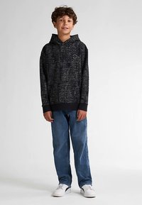 Schwarzer Kapuzenpullover mit strukturiertem, kontrastierendem grafischem Muster. Kombiniert mit hellblauen Jeans und weißen Turnschuhen. Legerer Schnitt und Stil.