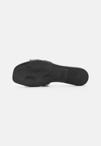 Black rubber outsole with textured surface, rectangular shape, and slight arch. Brown leather straps with stitching details above the sole.