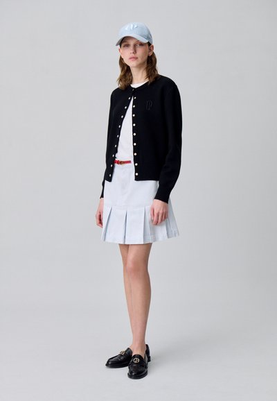 Cardigan nero con bottoni dorati, camicia bianca, gonna plissettata azzurro chiaro e mocassini neri con accessori dorati. Cappellino da baseball azzurro chiaro.