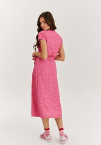 Růžové midi šaty s květinovým vzorem a krátkými rukávy, staženým pasem a sukní, která sahá pod lýtka, doplněné o růžové tenisky.