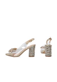 Transparante slingback hakken met een goudaccent op de doorzichtige band. Blokhak versierd met gouden en heldere edelsteen details.