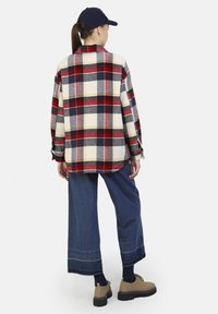 Rød, marineblå og gulternet overskjorte lavet af flanell, parret med brede jeans og beige snørebåndssko. Bagfra set med kasket.