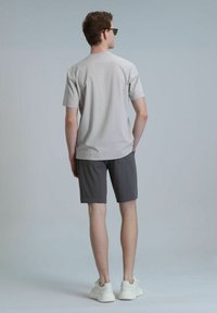 T-shirt gris clair à manches courtes, associé à un short gris foncé et des baskets blanches. Design simple et coupe décontractée, vu de dos.