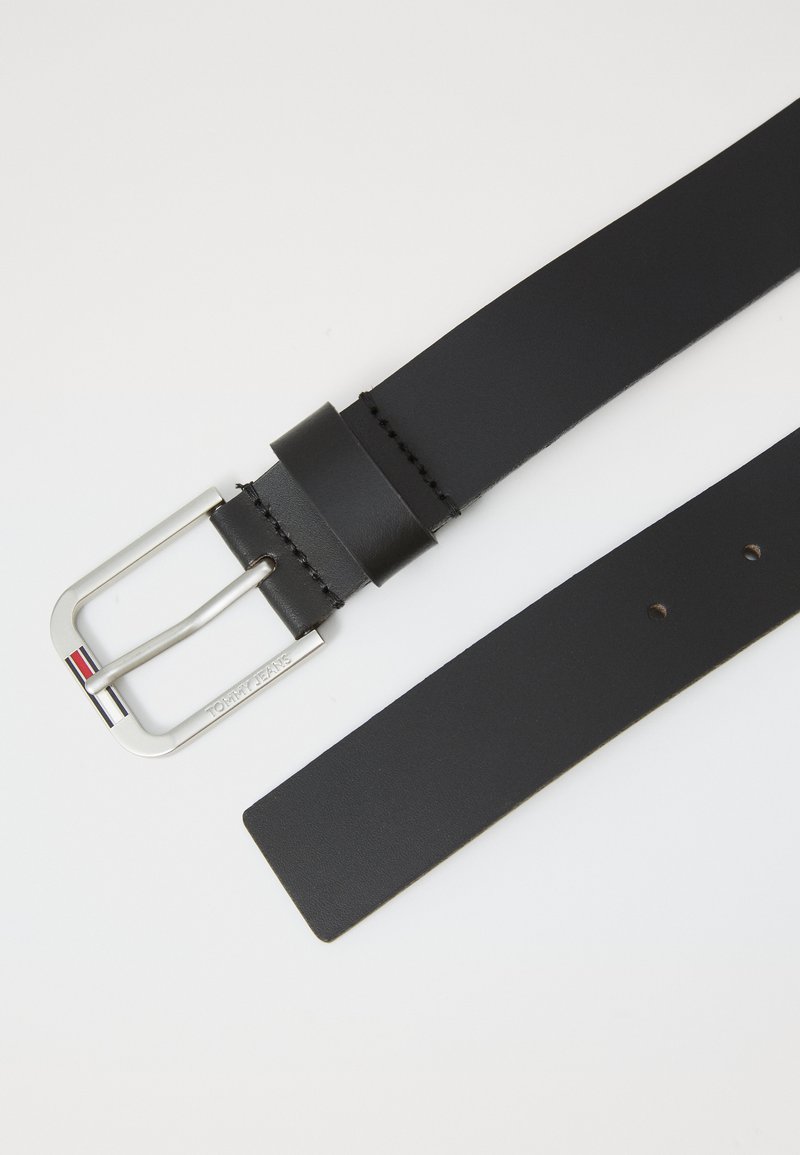 Cinturón de cuero negro con hebilla rectangular plateada que presenta pequeñas franjas en rojo, blanco y azul, y la grabación "TOMMY JEANS."