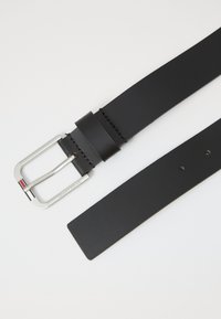 Cintura in pelle nera con fibbia rettangolare d'argento incisa con la scritta "Tommy Jeans" e piccolo dettaglio a strisce rosse, bianche e blu sulla fibbia.