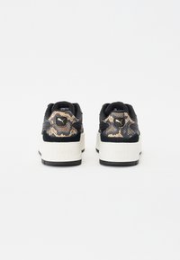 Schwarze Sneaker mit metallisch-goldenem Schlangenprint-Detail auf der Ferse, weißer Plattform-Mittelsohle und strukturiertem schwarzen Sohlen.