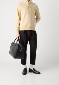 Sudadera beige con capucha, pantalones negros con pliegues, bolsa de cuero negra, mocasines negros y calcetines blancos; diseño minimalista y texturas suaves.